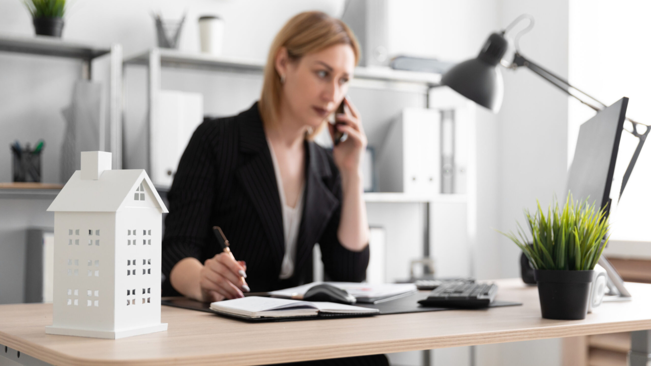 Beautiful young girl standing in a bright office near the desktop. The girl has blond hair. She is wearing a light blouse and a striped suit. photo with depth of field