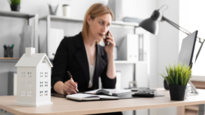 Beautiful young girl standing in a bright office near the desktop. The girl has blond hair. She is wearing a light blouse and a striped suit. photo with depth of field