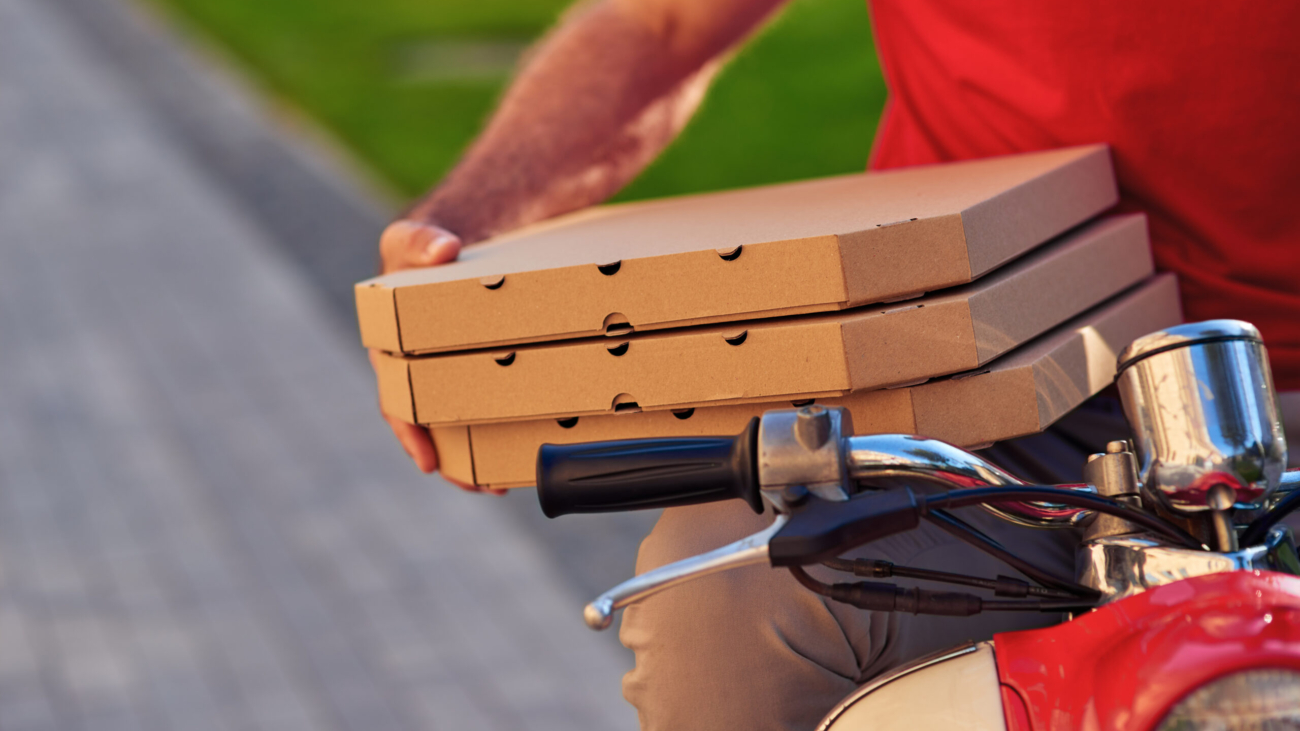 Courier in red uniform sitting on scooter and holding pizza boxes, selective focus. Food delivery concept