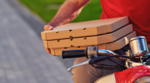 Courier in red uniform sitting on scooter and holding pizza boxes, selective focus. Food delivery concept